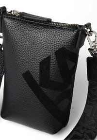 Černá kožená kabelka přes rameno s texturovaným povrchem, s velkým logem v matné černé a vzorovaným nastavitelným popruhem. Uzavírá se nahoře na zip.