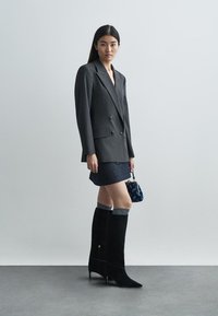 Kahekordse nööpimisega hall triibuline jakk, teksaseelik, põlvekõrgused mustad seemisnahast saapad, hallid kootud sokid, väike tumesinine käekott.