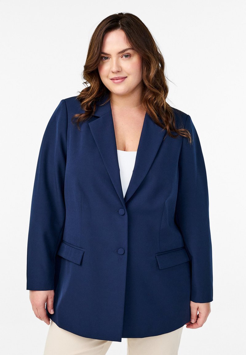 Tummansininen räätälöity bleiseri, jossa on notch-lapeli, yksittäinen nappikiinnitys ja kaksi etutaskua. Sileä kangas ja rakenteellinen istuvuus.