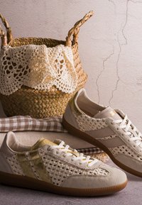 Baskets beige tissées avec des accents dorés placées près d'un panier tissé contenant un tissu crocheté crème et un tissu à carreaux plié.