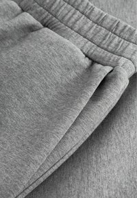 Szürke melegítőnadrág kiemelve, amely puha anyagú, rugalmas derékpánttal és hajtással a zseb környékén.