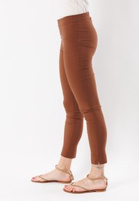 Leggings marroni con una texture liscia, design aderente e lunghezza alla caviglia, dotati di una vita e spacchi all'orlo. Abbinati a sandali piatti.