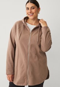 Brown zip-up hoodie with a hood, long sleeves, and kangaroo pocket. Smooth texture and relaxed fit. White inner layer visible.