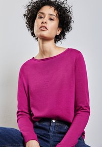 Fuchsia Langarm-Strickpullover mit Bootsausschnitt, gerippten Bündchen und weicher Textur, kombiniert mit dunkelblauen Jeans.
