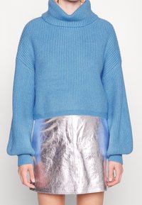 Pullover in maglia chunky di colore azzurro chiaro con dolcevita alto e spalle scese, abbinato a una mini gonna metallica argentata brillante.