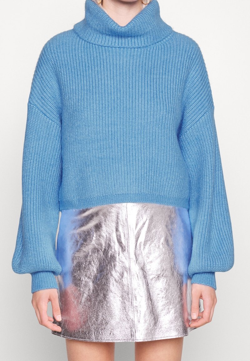 Pullover in maglia chunky di colore azzurro chiaro con dolcevita alto e spalle scese, abbinato a una mini gonna metallica argentata brillante.