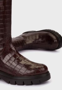 Botas de cuero marrón hasta el tobillo con textura de cocodrilo, punta redondeada, suela negra resistente y detalles de costura sutiles, diseñadas para la durabilidad.