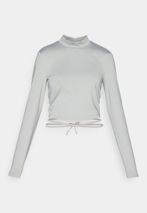 Svijetlosiva dugosleeve crop majica s lažnom kragnom. Izrađena od glatkog, rastezljivog materijala s vezicom na rubu.