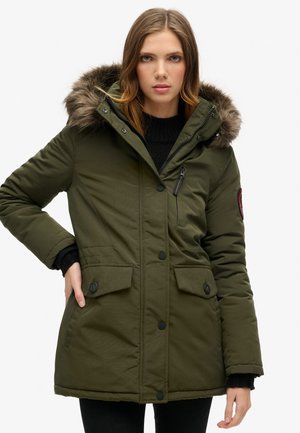 Olijfgroene parka jas met een met bont gevoerde capuchon, ritssluiting, grote voorzakken en knoopaccenten. Heeft een gewatteerde textuur.