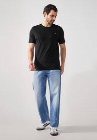 Svart t-skjorte med korte ermer og rund hals, kombinert med lyseblå denimjeans. Modellen har på seg hvite og svarte joggesko.