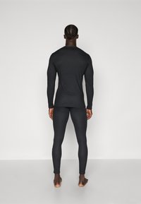 Maglia termica nera a maniche lunghe e leggings, design aderente, texture liscia, costruzione senza cuciture, con cuciture visibili all'orlo.