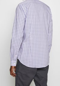 Camicia a maniche lunghe di colore viola chiaro con motivo a quadretti. Realizzata in cotone, con orlo curvo e dettagli con bottoni sui polsini.