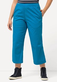 Turquoise, cropped broek met een elastische tailleband, zijzakken en een gladde textuur, gecombineerd met zwarte hoge sneakers.