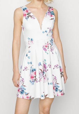Hvid ærmeløs kjole med dyb V-udskæring og blomster i lyserød, lilla og blå, tætsiddende ved taljen og udstående i en kort nederdel.