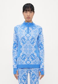 Light blue pullover with a zip neck, featuring white geometric patterns. Long sleeves with ribbed cuffs, made from a soft knit fabric.