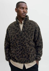 Fleece pullover in bruin met zwarte luipaardvlekken. Heeft een hoge kraag en een halve rits, een losse pasvorm en een zachte textuur.