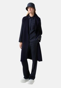 Navy trench coat with open front, paired with a matching shirt and pants. Accessories include a quilted hat and white chunky sneakers.