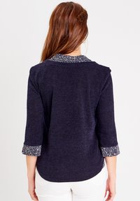 Marineblaue Bluse aus strukturiertem Stoff, mit Dreiviertelärmeln und kontrastierendem, floral gemustertem Besatz an Kragen und Manschetten.