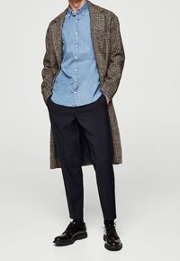 Brauner karierter langer Mantel über einem hellblauen Hemd mit Knöpfen, dunkle Hose und glänzende schwarze Schuhe. Verfügt über eine lockere Passform und ein geschichtetes Design.