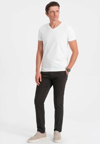 Bílé tričko s krátkým rukávem a výstřihem do V, kombinované s tmavými slim-fit kalhotami a světlými teniskami. Jednoduchý design s přiléhavým střihem a hladkou texturou.