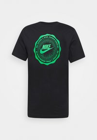 Černé bavlněné tričko s kulatým zeleným grafickým vzorem uprostřed, na kterém je text "Nike", vycházející linie a detaily značky kolem okraje.