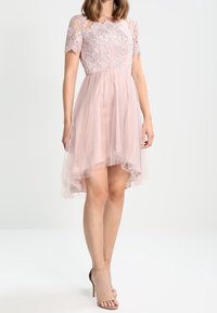 Růžové tylové šaty s přiléhavým korzetem a krátkými krajkovými rukávy. Obsahují vyšívané květinové detaily a lem v asymetrickém střihu.