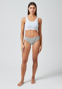 Grauer Baumwoll-BH mit Rundhalsausschnitt, kombiniert mit grauen Hipster-Slips mit Spitzenakzenten. Das Model steht barfuß vor einem schlichten Hintergrund.