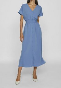 Sininen, polveen ulottuva mekko kevyestä kankaasta, jossa on V-kaula-aukko, lyhyet hihat, napitettava etuosa ja kiristetty vyötärö. Yhteensopivat korkokengät.