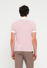 Άσπρο πόλο μπλουζάκι με κοντά μανίκια και κόκκινες οριζόντιες ρίγες, με κλασικό γιακά και εφαρμοστή σιλουέτα. Απλή σχεδίαση στην πλάτη.