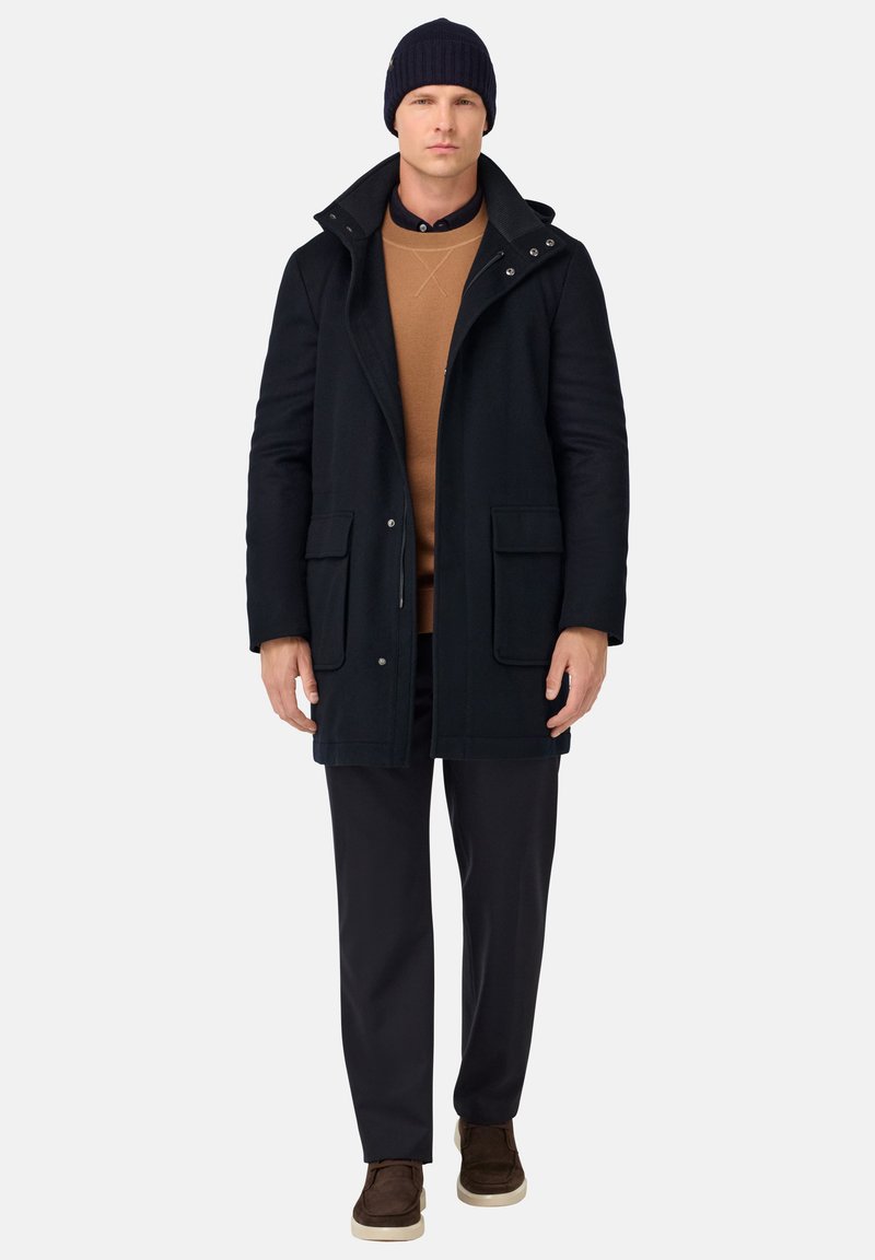 Mornarska bunda iz volnenega mešanice z visokim ovratnikom, dvema sprednjima žepoma in gumbnimi detajli; rjava jopica in temni hlače; rjavi copati.