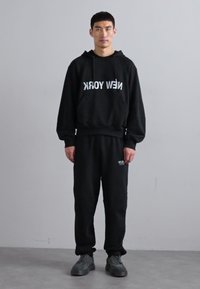 Czarna bluza z kapturem z napisem "NEW YORK" oraz czarne spodnie dresowe. Oba elementy wykonane z miękkiego materiału, luźny krój i minimalistyczny design.