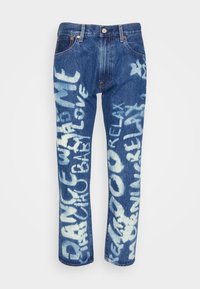 Pantalones vaqueros de mezclilla azul claro con un ajuste relajado, adornados con texto y diseños pintados en spray en blanco. Estilo estándar de cinco bolsillos y cierre de botón.