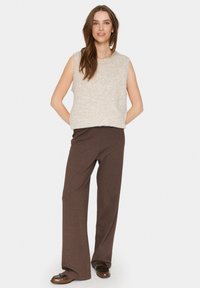 Kremasti bezrukavni top od teksturiranog materijala u kombinaciji s smešnim širem pantalonama; outfit se odlikuje opuštenim krojem, mekanim materijalom i minimalističkim dizajnom.