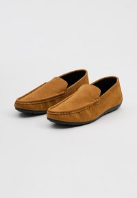 Mocasines de ante marrón con una textura suave, que presentan una puntera redonda, detalles de costura y una suela de goma negra para un buen agarre.