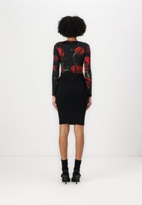Černý top s dlouhým rukávem a potiskem červené růže, spárovaný s přiléhavou černou žebrovanou sukní. Outfit obsahuje strukturovaný, elastický design a vysoké podpatky.