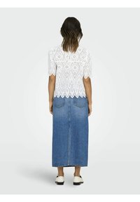 Weiße Bluse aus Lochstickerei mit kurzen Ärmeln und gewelltem Saum, kombiniert mit einem langen blauen Jeansrock mit Rückentaschen und geradem Schnitt.