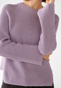 Light purple knitted sweater with a ribbed texture, wide sleeves, and a crew neckline. Features a seam detail along the back.