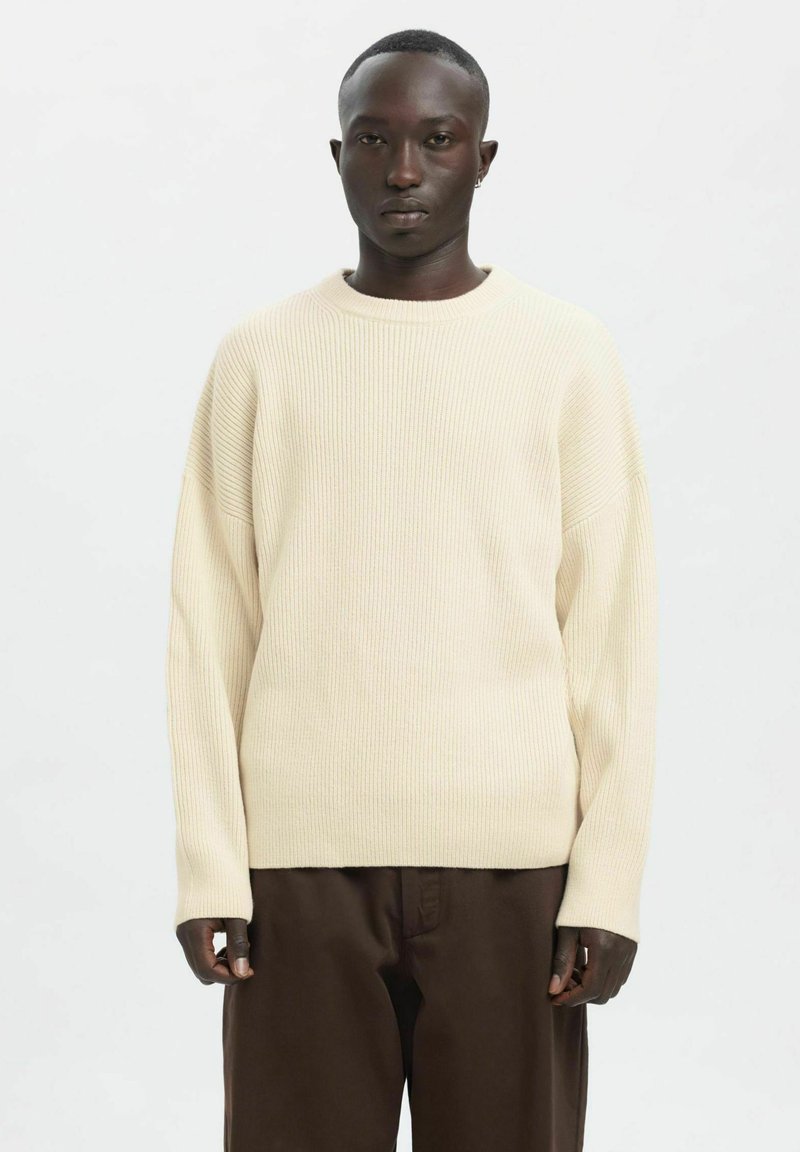 Kooretoonist soonikkoes kampsun ümarate kaeluse ja langevate õlgadega, kombineeritud pruunide pükstega; pehme tekstuur, lihtne disain ja lõdvestunud istuvus.