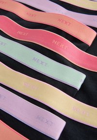 Horizontal pastel-colored fabric bands with the word "NEXT" embroidered repeatedly, arranged on a black surface.