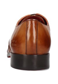 Zapato de vestir de cuero marrón con un acabado suave, punta redondeada, suela negra baja y acentos rojos en el interior. Presenta una marca en el talón.