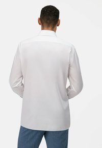 Camicia bianca a maniche lunghe con colletto classico e texture liscia. Presenta un orlo dritto e cuciture delle spalle arrotondate.