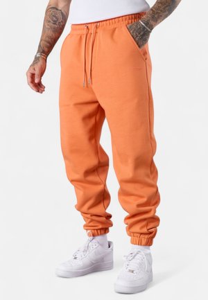 Pantalons de survêtement orange avec des poignets élastiques et une taille à cordon de serrage. Confectionnés en tissu doux, ils possèdent des poches latérales et des détails de marque subtils.