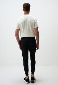 Kurzärmliges, Rundhals, weißes Baumwoll-T-Shirt kombiniert mit schwarzen Slim-Fit-Hosen und schwarzen Sportschuhen mit dunklen Sohlen.