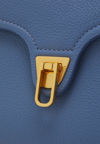 Niebieska torebka ze skóry o fakturze, z metalowym złotym zapięciem w kształcie prostokątnego otworu, podkreślonym kontrastującym przeszyciem.