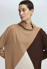 Pull en color-block marron et beige avec un col haut et replié. Fabriqué en matériau tricoté doux, présentant un motif triangulaire dans des tons atténués.