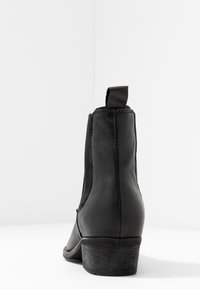 Bottines en cuir noir avec des panneaux élastiques sur les côtés, une languette de tirage et un talon bas texturé. Fini lisse et design à bout arrondi.