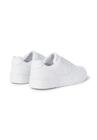 Witte sportieve sneakers hebben een glad leren bovenwerk, geperforeerde details, een logo op de zijkant en een rubberen zool met gestructureerde accenten.