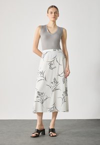 Grå ärmlös topp med v-ringning, tillsammans med en vit midikjol med svart blommönster, kompletterad med svarta klacksandaler.