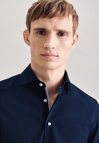 Camicia blu navy con colletto, caratterizzata da bottoni bianchi e un dettaglio a quadretti lungo la patta. Realizzata in tessuto morbido.