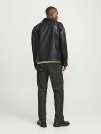 Chaqueta de cuero negro con cuello de presión, combinada con jeans de mezclilla oscura. Costuras detalladas en los jeans y calzado negro.